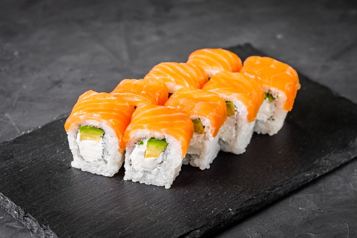 Philadelphia roll with salmon and avocado on a black stone plate.