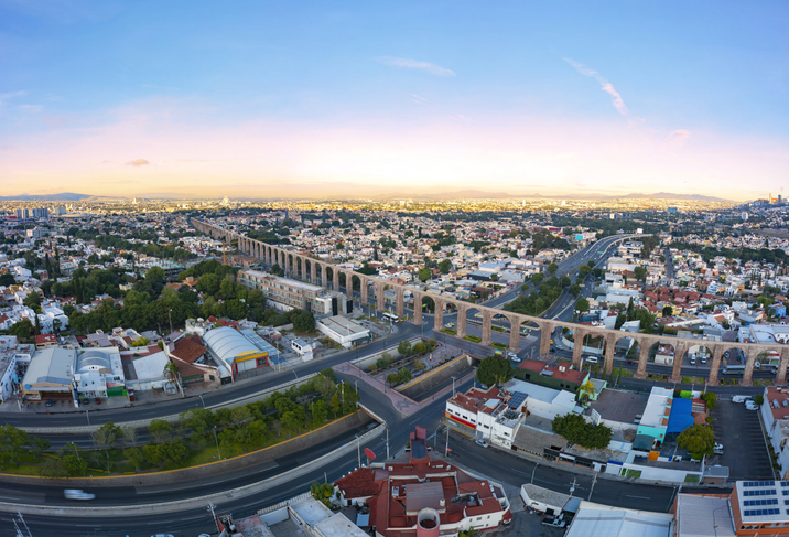 Aerial panoramic view over the famous Querétaro Aqueduct in the center of the city surrounded by buildings with a beautiful sunrise in the background